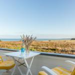 Terrasse mit zwei gelben Stühlen und Tisch. Blick auf Wasser und Feld.