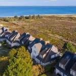 Häuser am Meer mit Grünflächen und Wiese im Hintergrund.