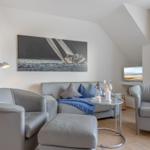 Wohnzimmer mit Sofa, zwei Sesseln und Wandbild. Holzboden und großes Fenster.