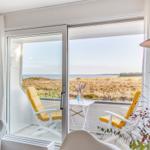 Terrasse mit zwei gelben Sesseln und Tisch. Blick auf Wasser und Grasland.