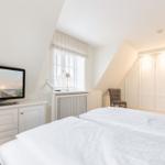 Schlafzimmer mit Bett, TV und Kleiderschrank. Fenster mit Vorhang und Stuhl.