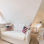 Schlafzimmer mit Sofa, Bett und Fenster unter Dachschrägen.