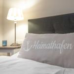 Bettkopfteil mit Kissen, das Heimathafen schreibt.