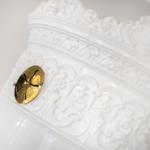 Weiße, verzierte Wand mit goldenem Ventil