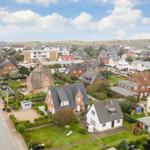 Dorf mit Häusern, Gärten und Straßen unter blauem Himmel.
