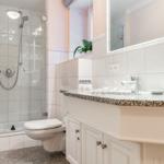Bad mit Dusche, Waschbecken und Toilette. Weiße Fliesen und Marmorarbeitsplatte.