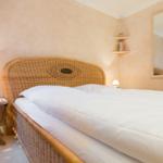 Schlafzimmer mit Rattanbett, Nachttisch und Spiegel an der Wand.