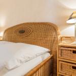Schlafzimmer mit Rattanbett und Nachttisch mit Lampe.