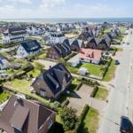 Aerial view of a coastal village with houses and green lawns near the sea.