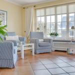 Wohnzimmer mit blau-weißen Sesseln, Glas-Tisch und Fenster mit Jalousien.