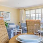 Esszimmer mit Blick auf Wohnbereich mit blau gestreiften Sesseln und Fenster mit Jalousien.