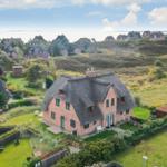 Haus mit Strohdach und Garten, Blick auf Strand und Hügel.