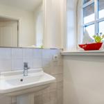 Badezimmer mit Waschbecken, Spiegel und Fenster mit Segelboot.