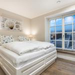 Schlafzimmer mit Blick auf Strand und Meer durch große Fenster.