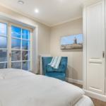 Schlafzimmer mit Blick auf Strand, blauer Sessel und weißer Kleiderschrank.