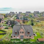 Dorfhaus mit Strohdach und Garten, Blick auf Meer und Landschaft.
