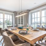 Esszimmer mit langem Holztisch, Stühlen und großen Fenstern mit Blick nach draußen.