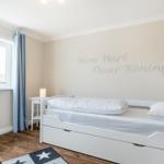 Schlafzimmer mit weißem Bett, Fenster und Wanddekoration.