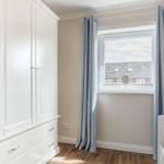 Schlafzimmer mit weißem Schrank, Fenster mit Vorhängen und Blick auf Dach