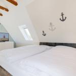 Schlafzimmer mit Dachbodenfenster, Bett und Fernseher.