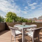 Terrasse mit Sitzgruppe und Holzgeländer. Blick auf Bäume und Häuser.