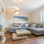 Wohnzimmer mit Sofa, Couchtisch und Seemotivskulptur. Fenster mit Strand-Schriftzug.