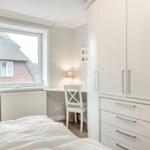 Bedroom with white desk, chair, and wardrobe. Window shows thatched roof house.