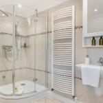Shower enclosure with glass, handheld shower, heater, and sink with mirror.