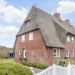 Red brick house with thatched roof and white gate