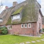 Red brick house with thatched roof and garden.