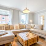 Living room with L-shaped sofa, wooden table, and windows.