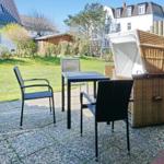 Terrace with table, three chairs, and lounge chair. Background: garden and houses.
