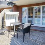 Terrace with table, chairs, and beach chair in front of house with windows.