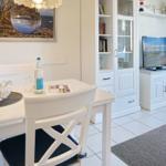 Dining area with white table and chairs, TV and bookcase in background.