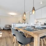 Essbereich mit Holztisch und Stühlen, Küche mit weißen Schränken und Esszimmer im Hintergrund.