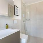 Bad mit Dusche, Waschbecken und Toilette. Fliesenwand und Spiegel sichtbar.
