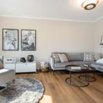 Wohnzimmer mit grauem Sofa, Holzboden und Wandbildern.