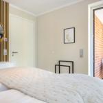 Schlafzimmer mit Bett, Spiegel und Zugang zu Balkon mit Stuhl