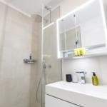 Badezimmer mit Dusche, Waschbecken und beleuchtetem Spiegelschrank.