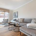 Wohnzimmer mit grauem Sofa, Couchtisch und Sessel. Holzboden und Fenster mit Rollladen.