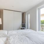Schlafzimmer mit Doppelbett, Kleiderschrank und Fensterblick auf Garten.