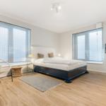 Schlafzimmer mit Bett, Fenstern und Sitzgelegenheit.