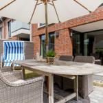Terrasse mit Tisch, Stühlen und Sonnenschirm. Hintergrund: rote Ziegelwand und Glasfront.