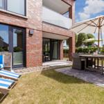 Terrasse mit Sitzgruppe, Sonnenschirm und Strandkörben vor einem Haus mit Backsteinfassade.