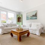 Wohnzimmer mit zwei weißen Sofas, Holzcoffee-Tisch und Wandbild.