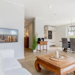 Wohn- und Essbereich mit Küchenzeile und TV. Holzmöbel und große Fenster.
