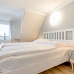 Schlafzimmer mit weißem Bett, Nachttisch und Fenster