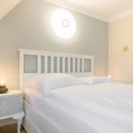 Schlafzimmer mit weißem Bett, Nachttisch und Wandlampe
