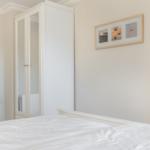 Schlafzimmer mit weißem Bett, Kleiderschrank und Wandbild.