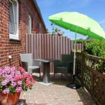 Terrasse mit grünem Sonnenschirm, Tisch, Stühlen und Blumenpflanzen.